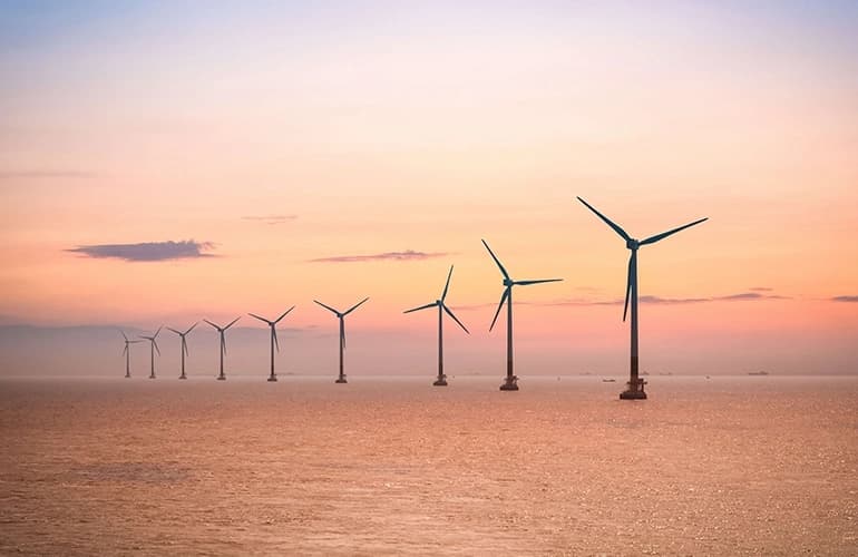 Offshore wind turbines at sea during sunset.
