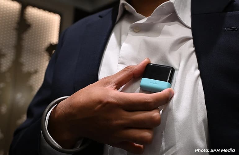 Close-up of a person holding a small wearable device against their shirt.