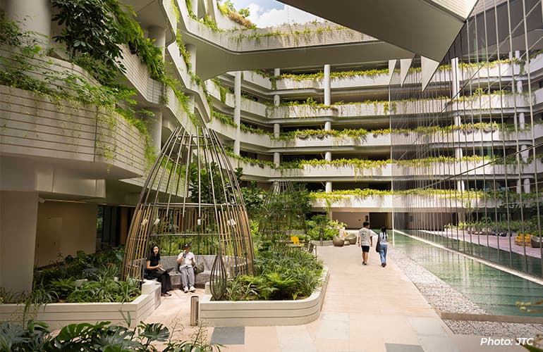 Interior courtyard of a modern green building featuring landscaped walkways, cascading plants, seating areas, and a reflective water feature.