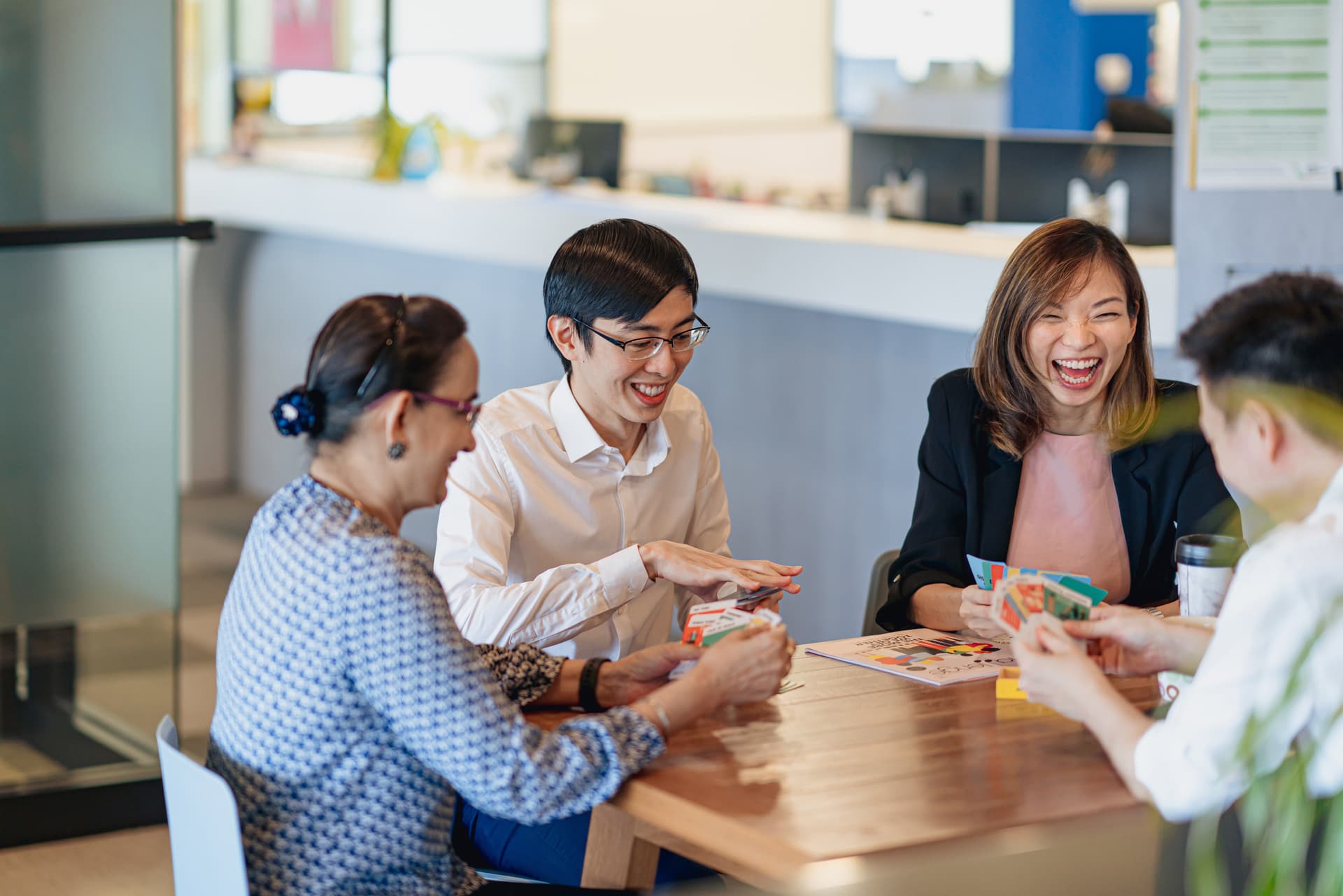 Colleagues laughing while playing cards at an office table.