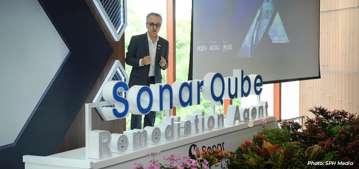 Speaker presenting SonarQube remediation technology at an industry event, standing beside a large SonarQube display with a presentation screen in the background.