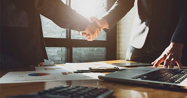 Two businesspeople shaking hands over documents.