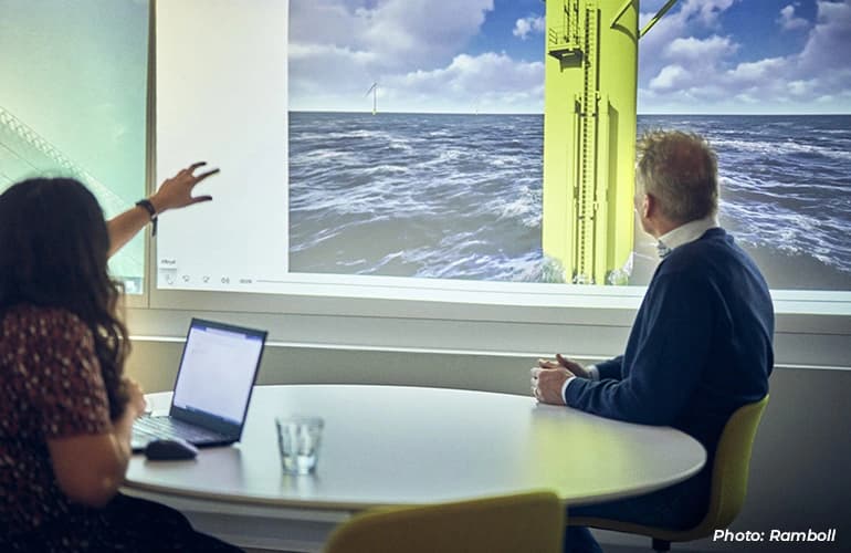 Two people in a meeting viewing an offshore wind energy presentation on a large screen.