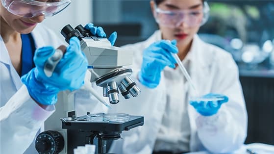 Lab scientist in protective gear using a microscope and pipette