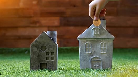 Hand placing a coin into a house-shaped piggy bank.