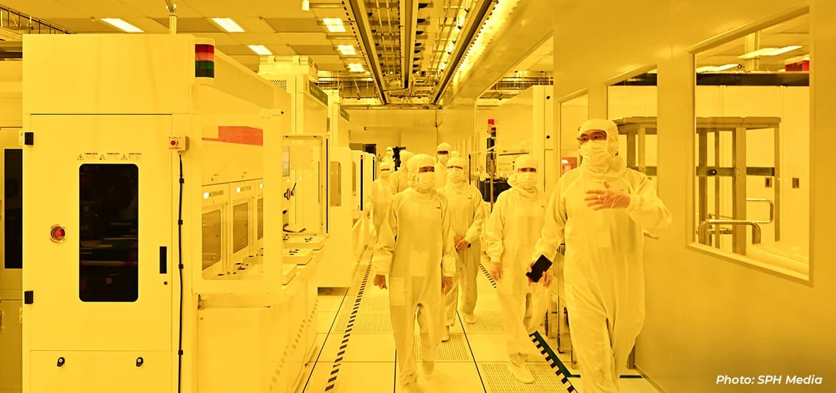 People in cleanroom suits walking through a semiconductor manufacturing facility.
