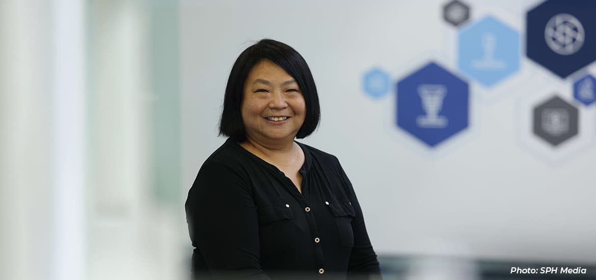 Woman smiling in an office setting, with abstract technology and innovation icons displayed on the wall in the background.