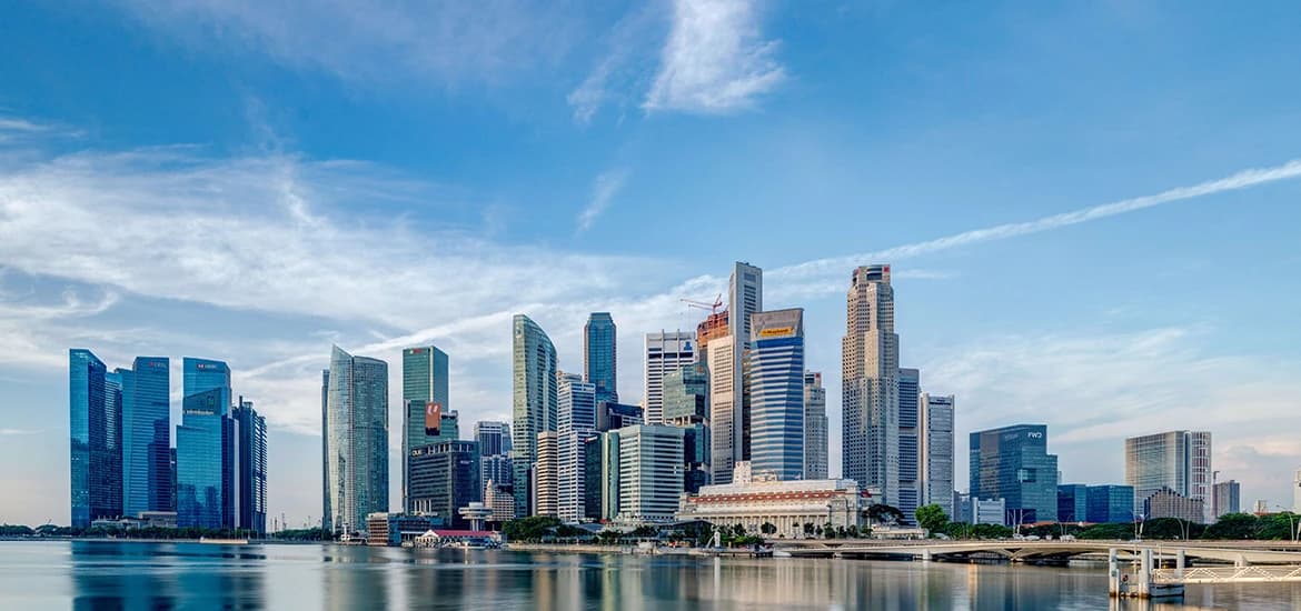 Singapore city skyline across Marina Bay under a blue sky.