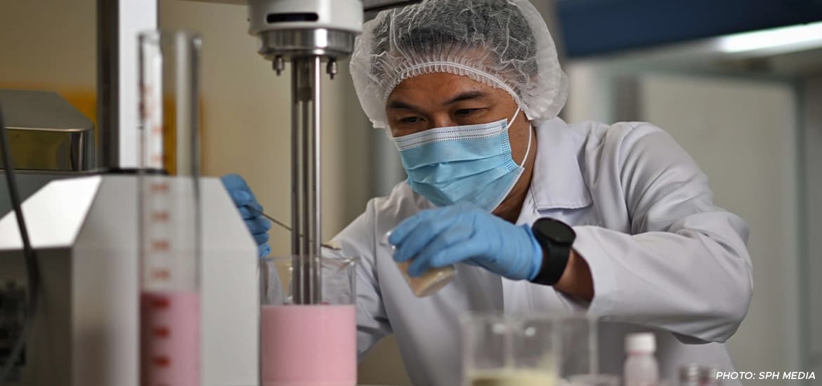 Scientist in protective gear carefully mixing ingredients in a lab, conducting a food formulation experiment with pink liquid.