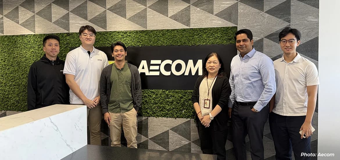 AECOM team members standing together in a modern office reception area, with an AECOM logo and greenery feature wall in the background.
