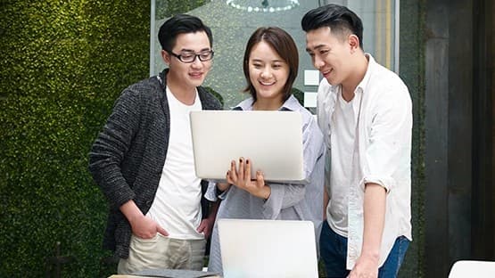 Three colleagues collaborating around a laptop.