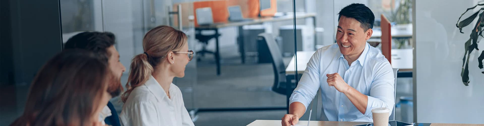 A man smiling and gesturing while talking with colleagues in an office meeting."