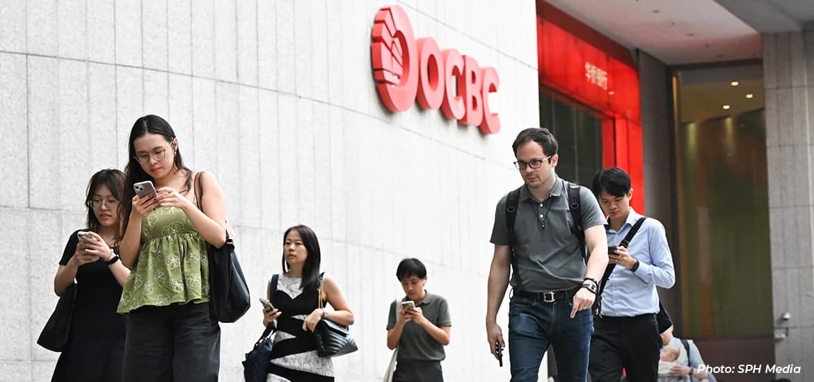 People walking past the OCBC building in Singapore’s central business district, many looking at their mobile phones while commuting.