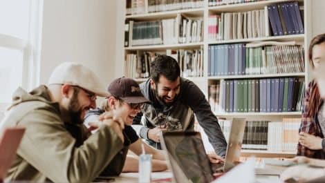 Colleagues laughing together at a laptop in a library.