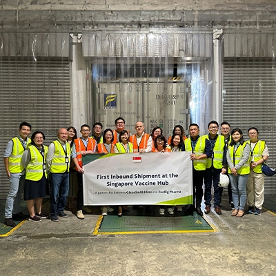 Group photo of staff in safety vests holding a banner reading 'First Inbound Shipment at the Singapore Vaccine Hub – A partnership between GlaxoSmithKline and Zuellig Pharma'
