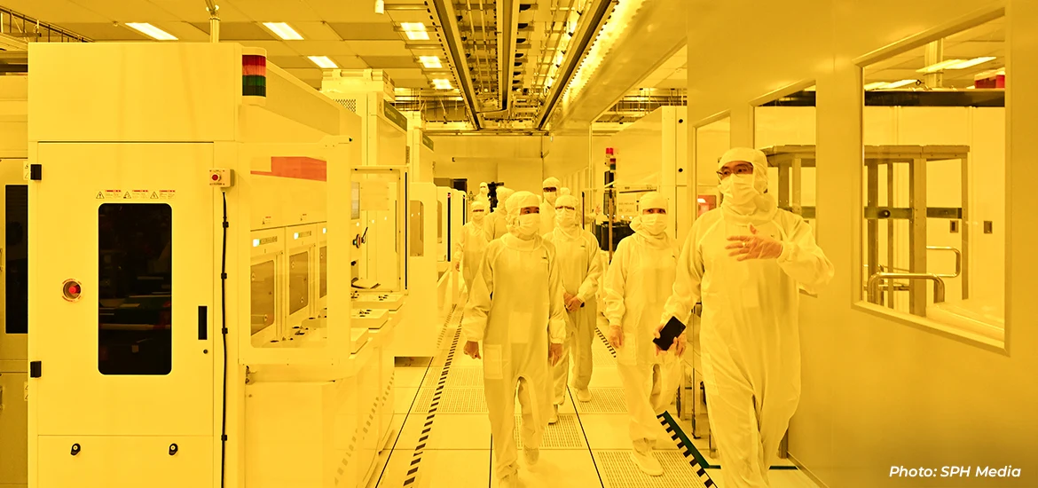 People in cleanroom suits walking through a semiconductor manufacturing facility.