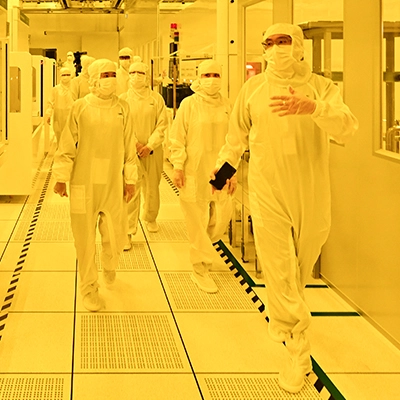 People in cleanroom suits walking through a semiconductor manufacturing facility.