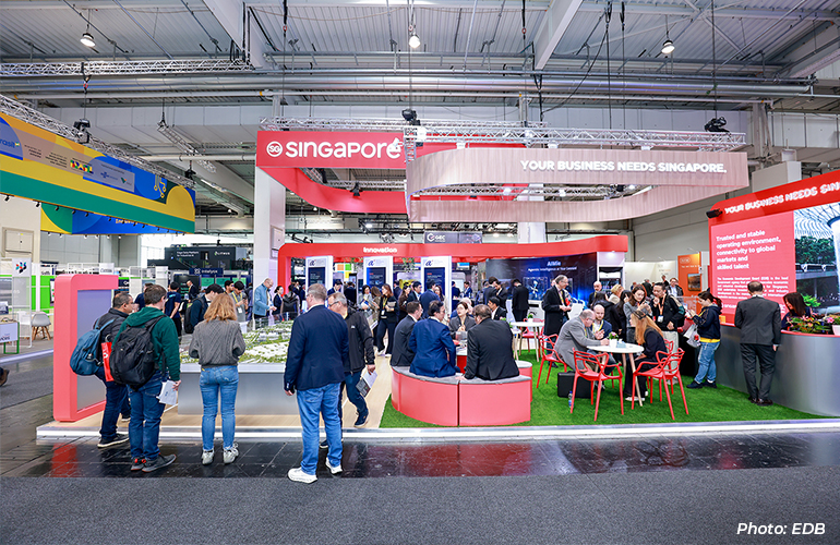 Visitors networking and exploring the Singapore pavilion at an international trade exhibition, featuring showcases on innovation, advanced manufacturing, AI, and business opportunities in Singapore.