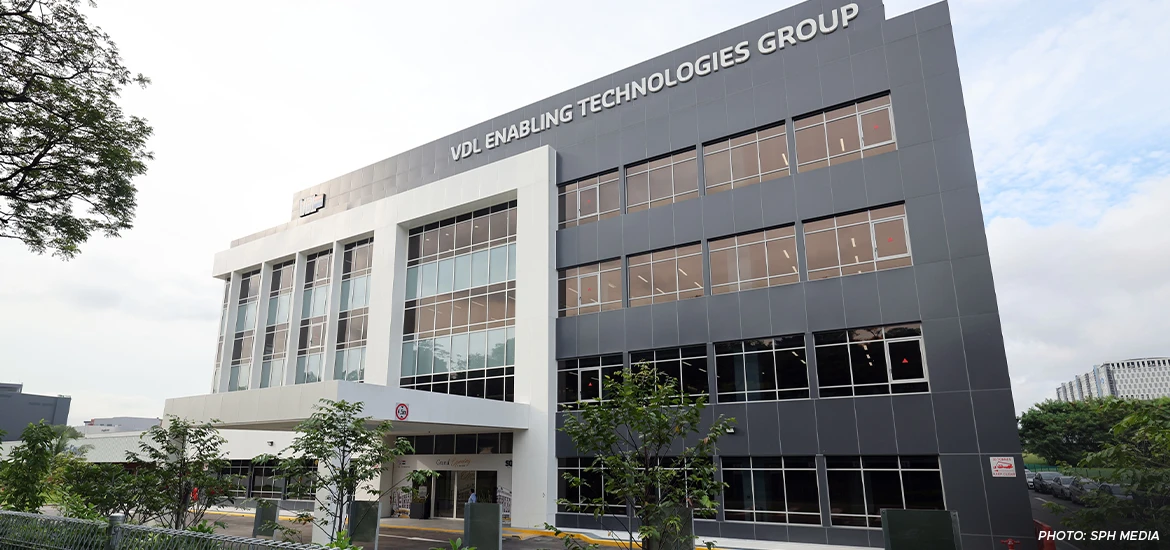 Exterior view of the VDL Enabling Technologies Group building, a modern multi-story facility with large glass windows and sleek gray paneling.