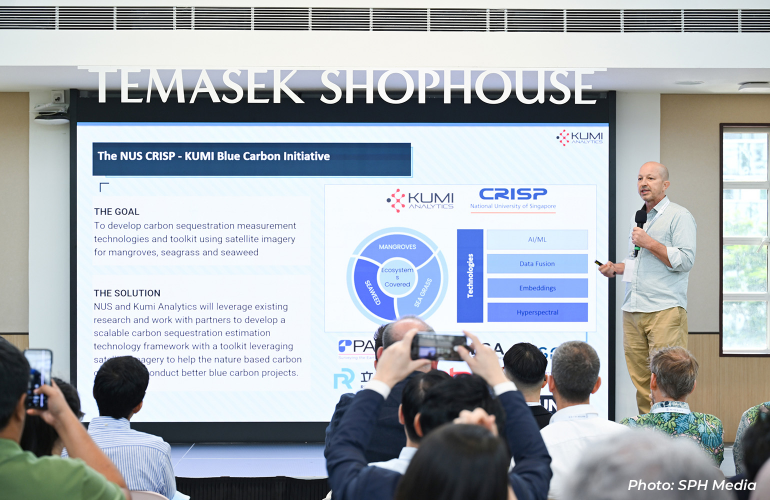 Speaker presenting the NUS CRISP–KUMI Blue Carbon Initiative at Temasek Shophouse, explaining the use of satellite imagery and AI technologies to support carbon sequestration projects for mangroves, seagrasses, and seaweed ecosystems.