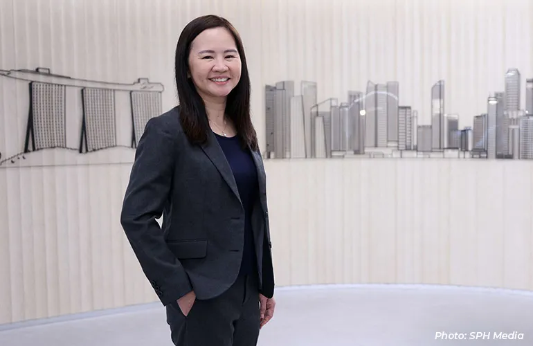 Woman in a dark business suit smiling, standing in front of a stylized city skyline backdrop.