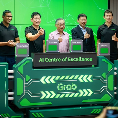 Group of five men giving thumbs up at the launch of Grab's AI Centre of Excellence, standing in front of a vibrant green digital-themed backdrop with labeled pillars for Community, Grabbers, Government, and Partners.