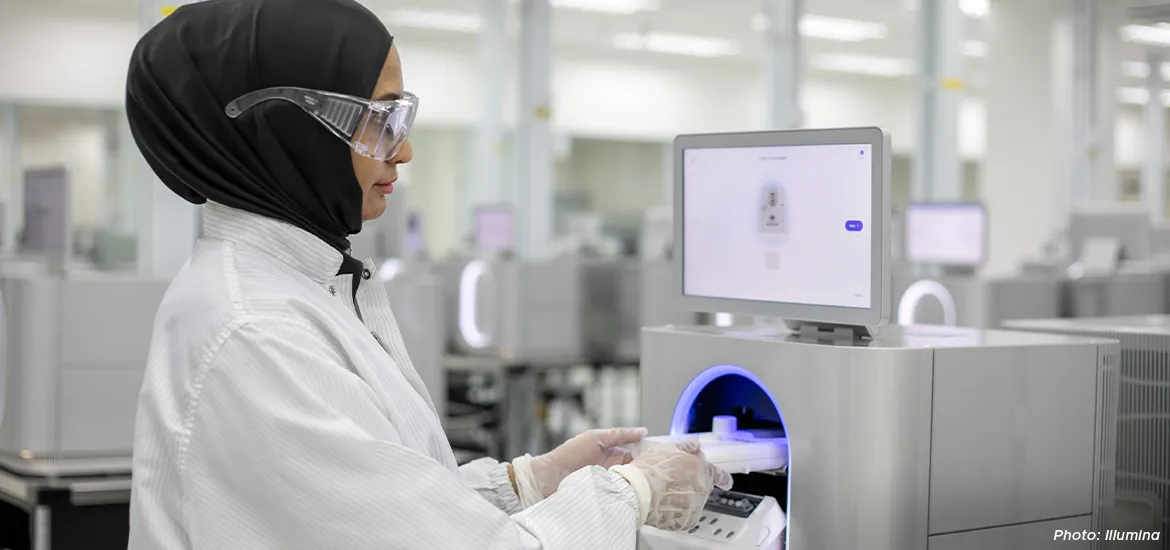 Scientist in a lab coat and safety goggles operating advanced laboratory equipment with a touchscreen interface inside a modern research facility.
