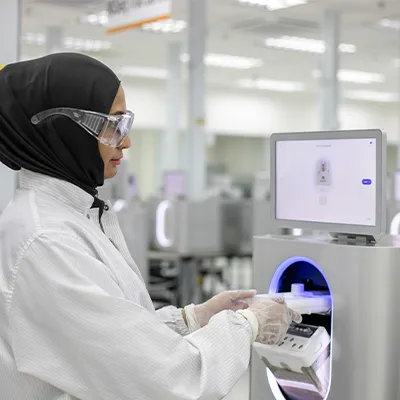 Scientist in a lab coat and safety goggles operating advanced laboratory equipment with a touchscreen interface inside a modern research facility.