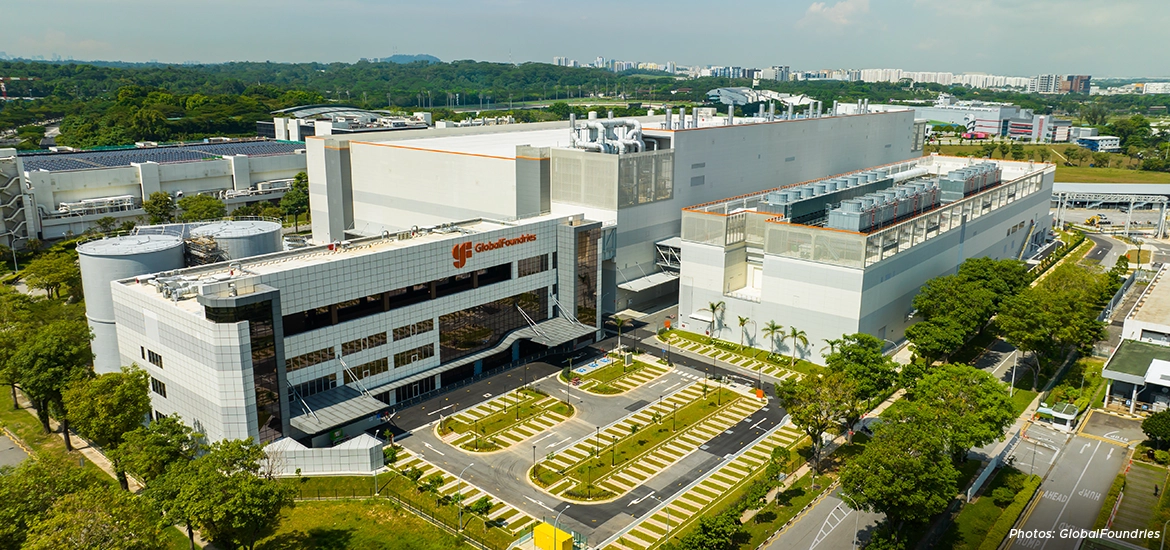 An aerial view of the GlobalFoundries semiconductor manufacturing facility in Singapore, featuring large fabrication buildings, advanced industrial infrastructure, and surrounding greenery.