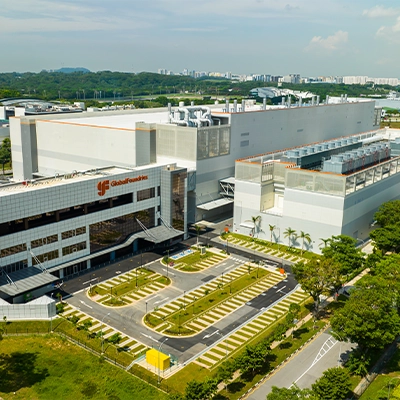 An aerial view of the GlobalFoundries semiconductor manufacturing facility in Singapore, featuring large fabrication buildings, advanced industrial infrastructure, and surrounding greenery.