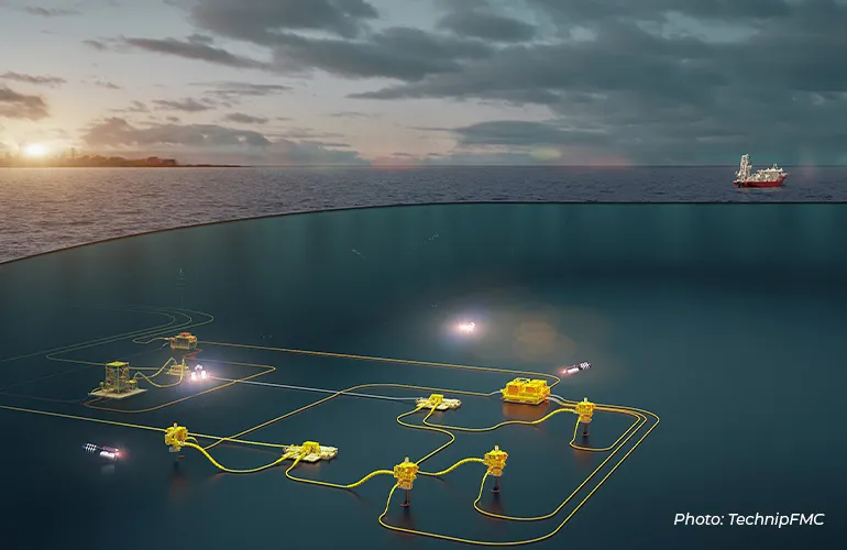 Subsea oil and gas production system with interconnected underwater equipment and pipelines, supported by an offshore drilling vessel at sunset.