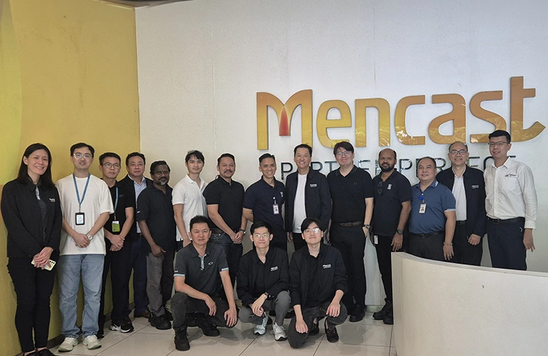 Group photo of the Mencast team standing in front of the company logo.