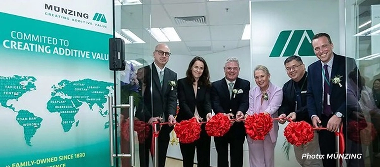 Münzing executives in formal attire cutting a red ribbon at an opening ceremony inside an office, with company branding displayed in the background.