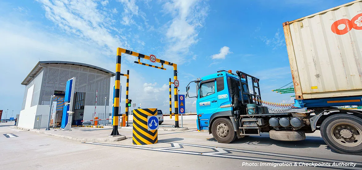 Container truck entering a checkpoint gate at a port or logistics facility under a clear blue sky.