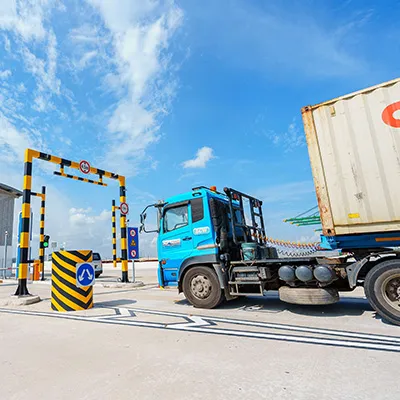 Container truck entering a checkpoint gate at a port or logistics facility under a clear blue sky.