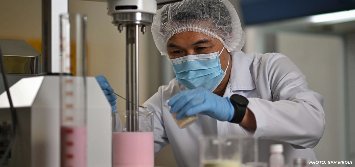Scientist in protective gear carefully mixing ingredients in a lab, conducting a food formulation experiment with pink liquid.