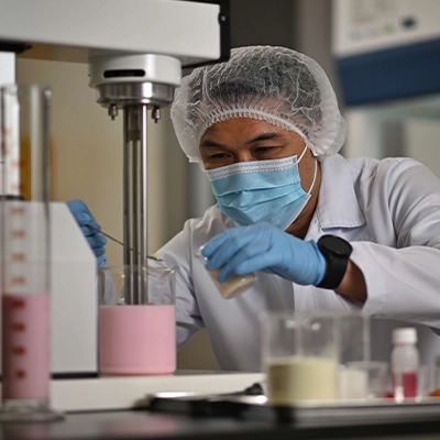 Scientist in protective gear carefully mixing ingredients in a lab, conducting a food formulation experiment with pink liquid.