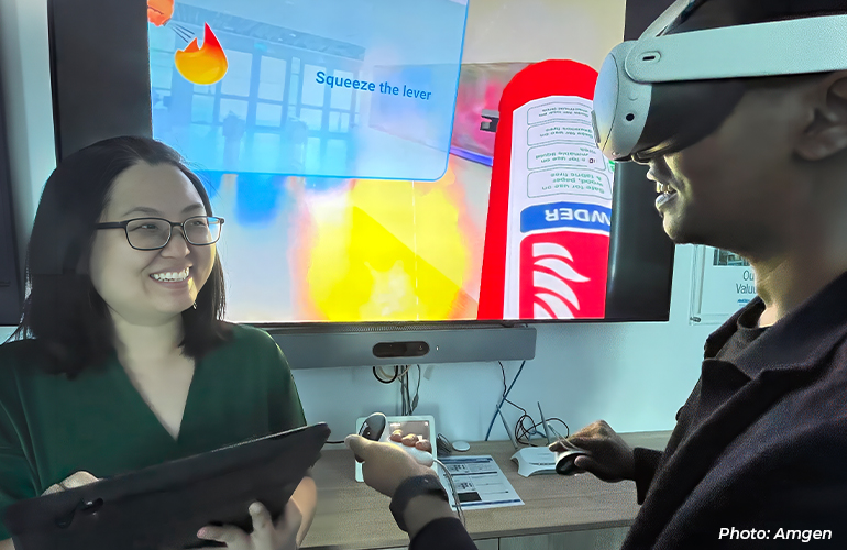 Employee using a virtual reality headset during an immersive training session, while a colleague observes and assists. A screen in the background displays a simulated fire safety scenario, demonstrating the use of digital technologies for workplace training and skills development.