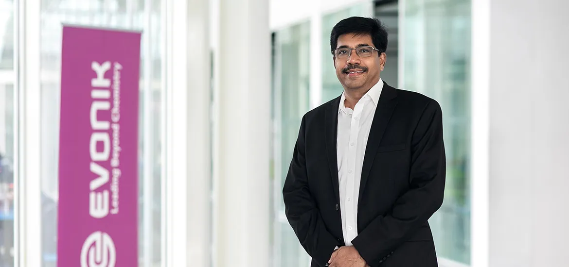 Professional portrait of a man in a suit standing in a bright office corridor beside an Evonik banner.