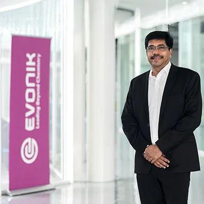 Professional portrait of a man in a suit standing in a bright office corridor beside an Evonik banner.
