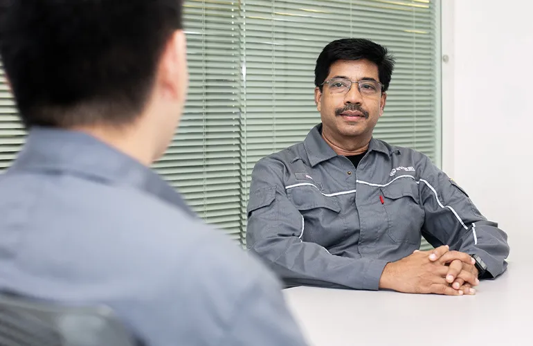 Man in a gray Evonik uniform sitting at a table and attentively listening to a colleague during a meeting.