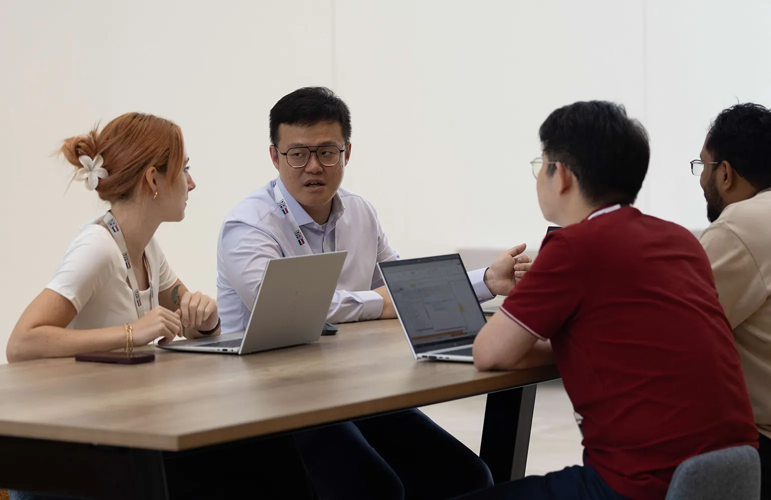 Four colleagues engaged in a serious discussion around a table with laptops open. A man in a white shirt speaks while the others—two men and a woman—listen attentively, creating a focused and collaborative work atmosphere.