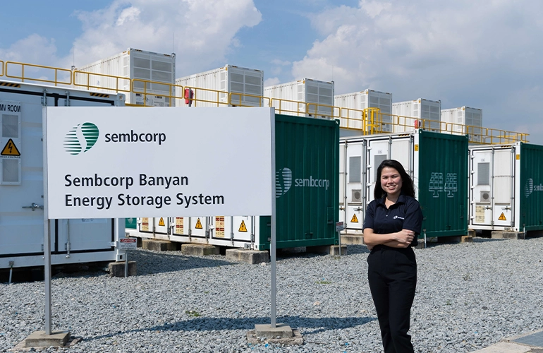 Woman standing beside Sembcorp Banyan Energy Storage System containers at an industrial site.