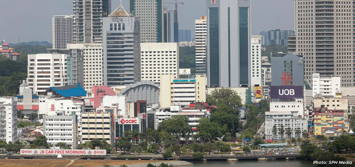 Cityscape of Johor Bahru, Malaysia, showing tall office buildings, banks, and hotels near the waterfront under clear skies.