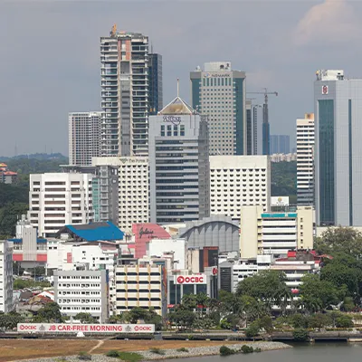 Cityscape of Johor Bahru, Malaysia, showing tall office buildings, banks, and hotels near the waterfront under clear skies.