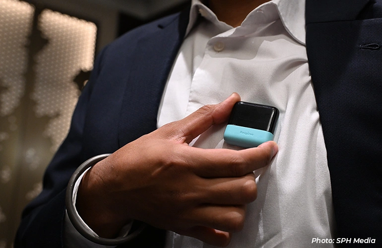 Close-up of a person holding a small wearable device against their shirt.