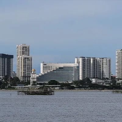 Cityscape of Johor Bahru with modern high-rise buildings and waterfront view under a clear blue sky.