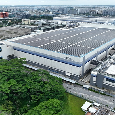 Micron semiconductor manufacturing facility in Singapore, featuring large cleanroom buildings and rooftop solar panels surrounded by greenery.