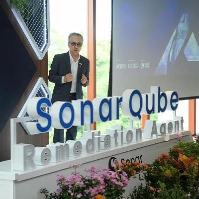 Speaker presenting SonarQube remediation technology at an industry event, standing beside a large SonarQube display with a presentation screen in the background.