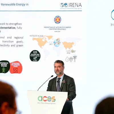IRENA Director delivers a keynote presentation at the Asia Clean Energy Summit, standing at a podium with IRENA and ACES logos displayed on a large screen highlighting renewable energy partnerships and regional cooperation.